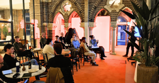 a group of people sitting at tables in a room with arches and red lights